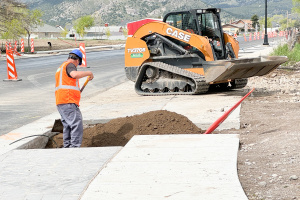 A landscape worker rakes dirt along Main Street. A skid steer is in the background