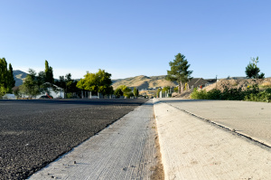 A straight, wide view of the newly completed 7300 West road in Herriman, featuring fresh asphalt with double yellow lines.